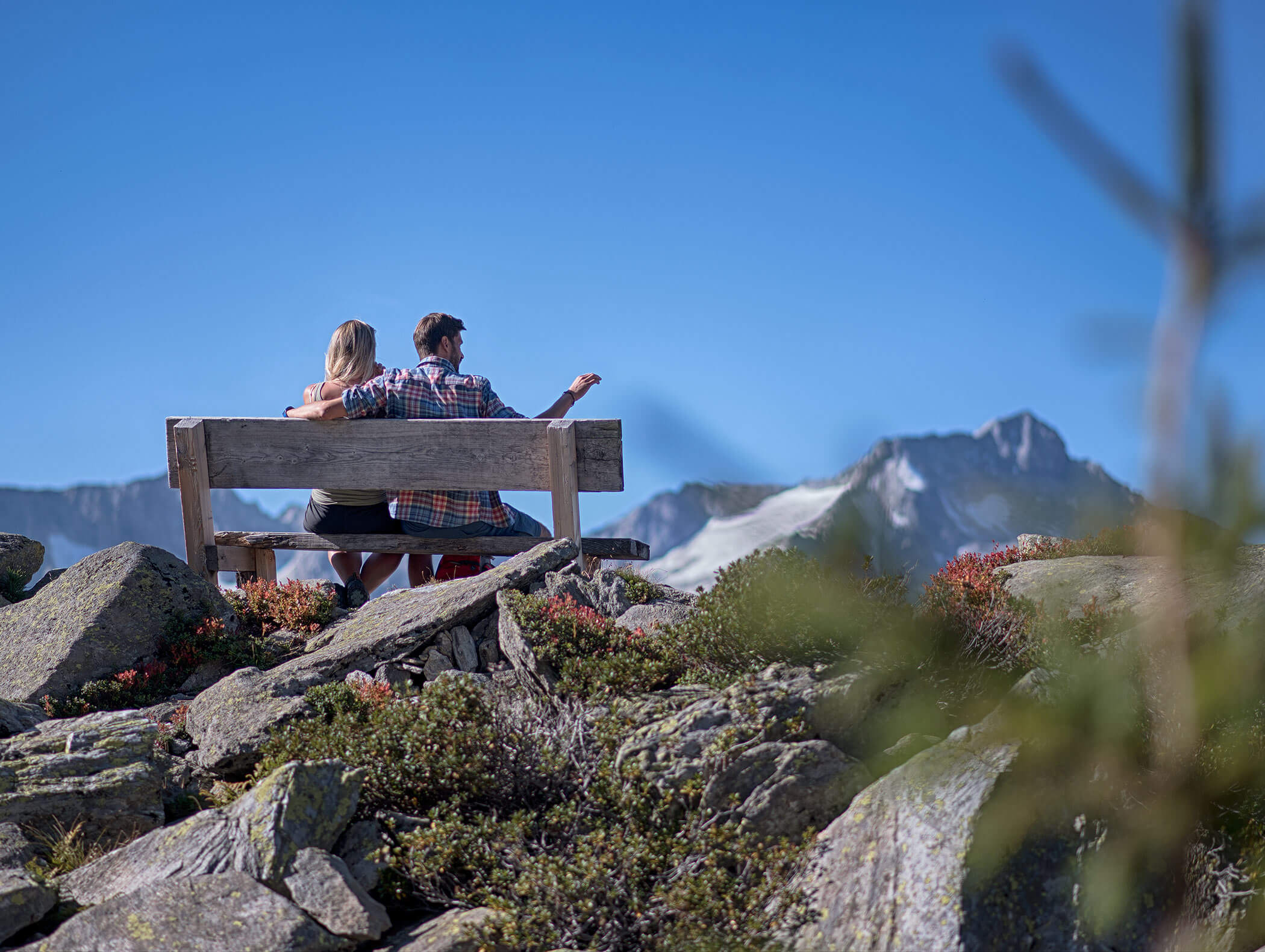 A couple sitting on a wooden bench enjoying the mountain scenery - Berghotel Alpenfrieden