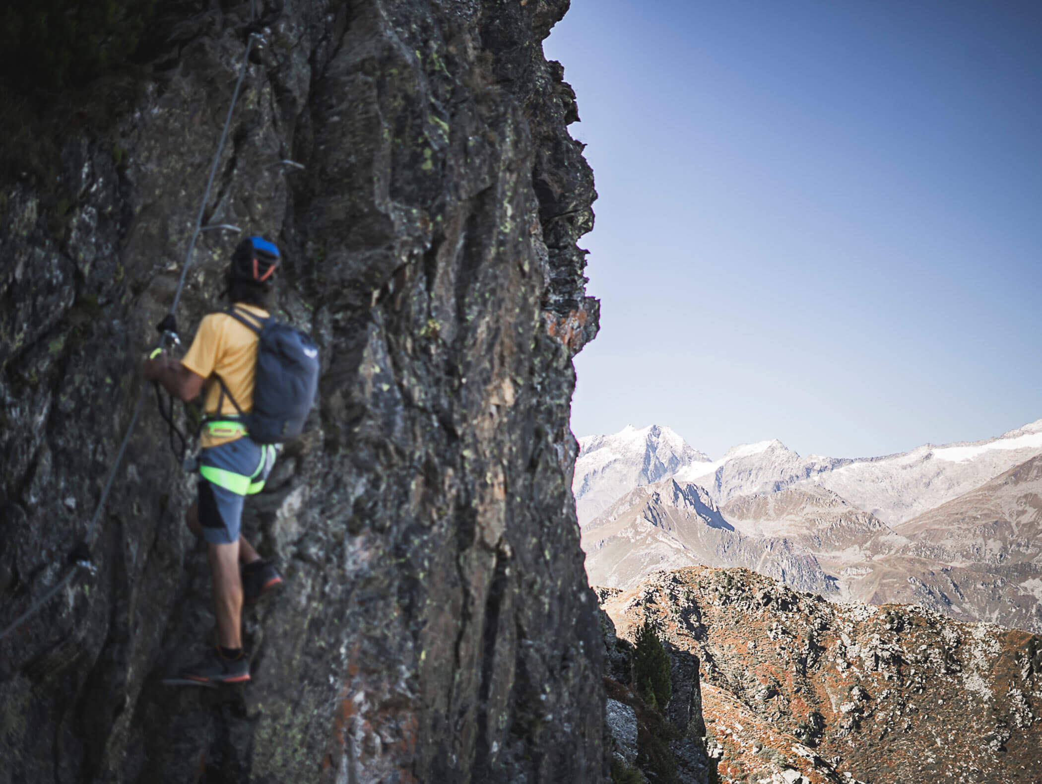 Man climbing a rock face, in the background a breathtaking mountain landscape - Berghotel Alpenfrieden