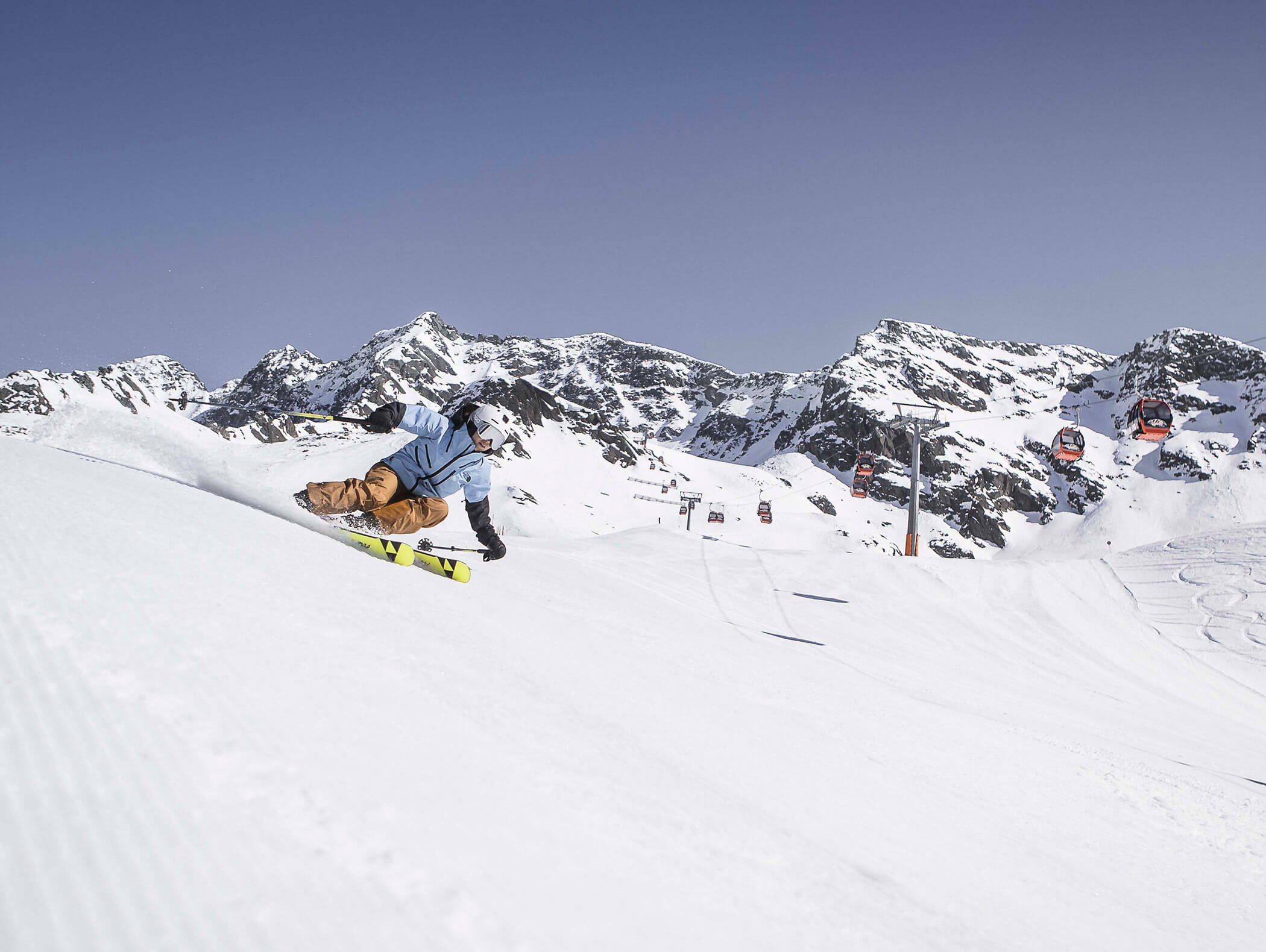 A man skiing on the freshly groomed slopes of the Speikboden ski area, with the red gondolas in the background - Berghotel Alpenfrieden
